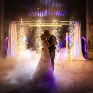 Couple de mariés s'embrassant sur la piste de danse entouré de fumée basse et de jets d'étincelles.