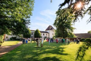 Vue d'ensemble des invites lors d'un cocktail de mariage en plein air dans le jardin d'un domaine a Macon sous un ciel bleu.