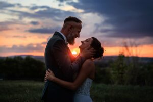 Portrait romantique d'un couple de maries s'enlacant tendrement devant un coucher de soleil flamboyant a la campagne.