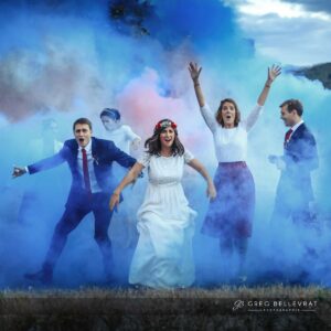 Les mariés et leurs amis posant avec enthousiasme au milieu de fumigènes bleus et roses.