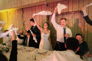 Les invités debout à table font tourner des serviettes blanches en l'air dans une ambiance de fête.