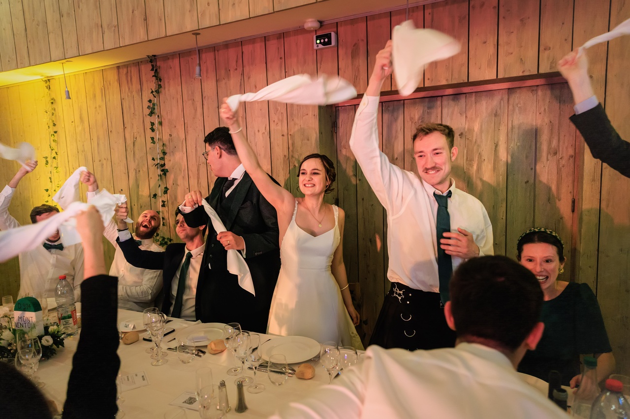 Les invités debout à table font tourner des serviettes blanches en l'air dans une ambiance de fête.