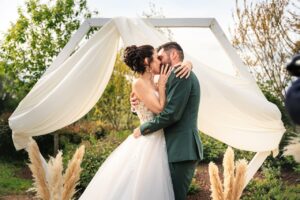 Les maries s'embrassent sous une arche de mariage moderne en plein air.