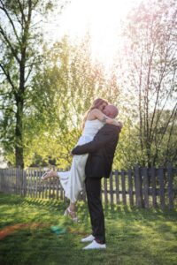 Le marie souleve la mariee dans ses bras pour un baiser passionne dans un jardin eclaire par le soleil couchant.