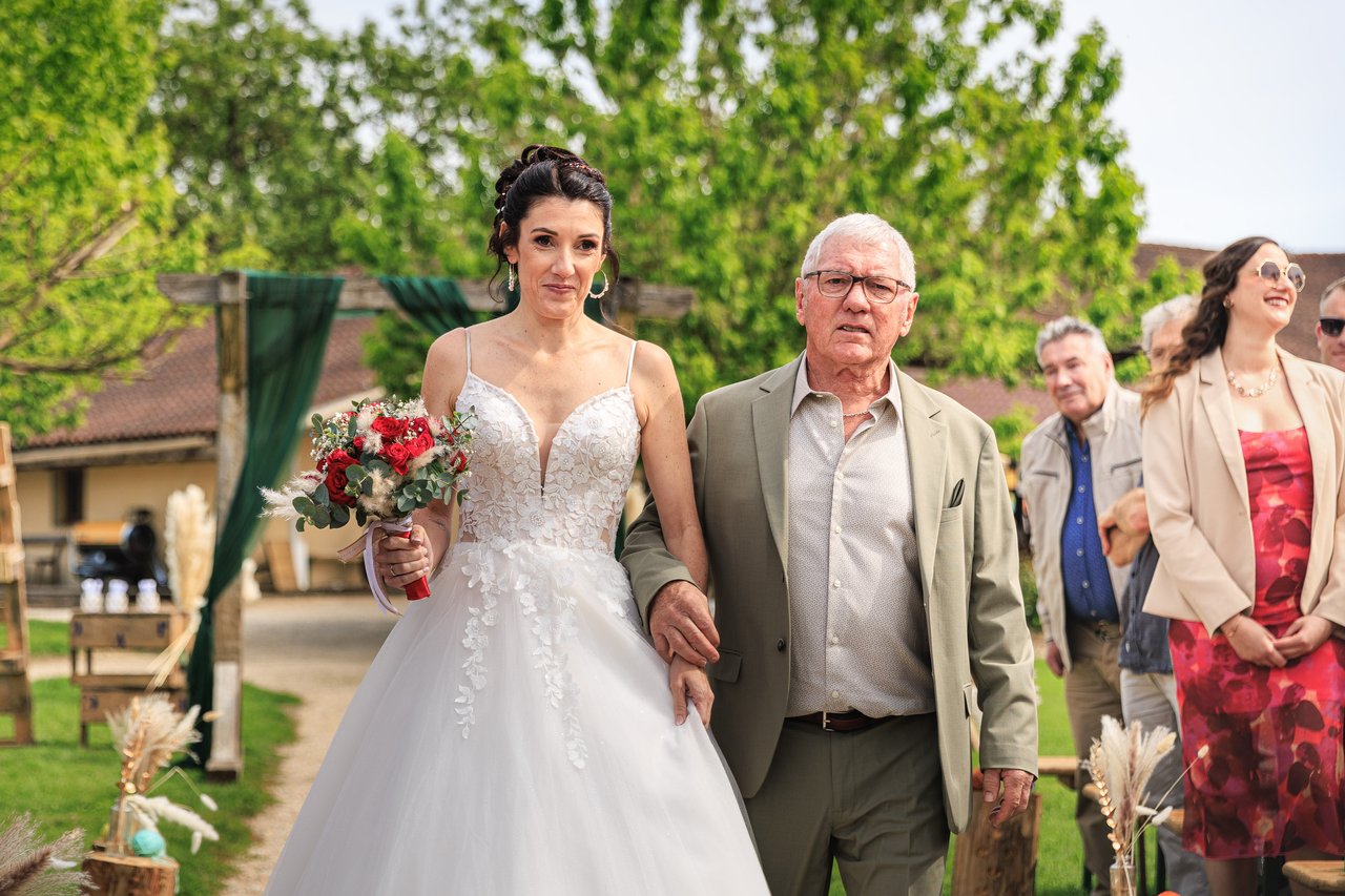 La mariee marche dans l'allee de la ceremonie accompagnee de son pere.