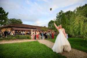 La mariee lance son bouquet de fleurs vers un groupe d'invitees en exterieur.