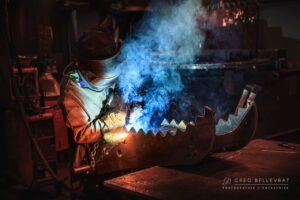 Reportage industriel à Villefranche-sur-Saône : photographe d'entreprise capturant un soudeur en action avec des jeux de lumière et de fumée dans un atelier de métallurgie.