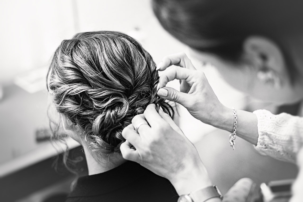 Vue rapprochée des mains d'une coiffeuse travaillant sur le chignon tressé de la mariée.