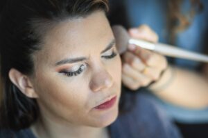 Gros plan sur le visage de la mariee pendant qu'une maquilleuse applique du fard a paupieres avec un pinceau.