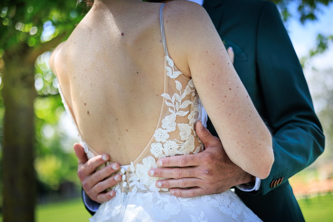 Gros plan sur le dos d'une robe de mariee en dentelle blanche avec les mains du marie.