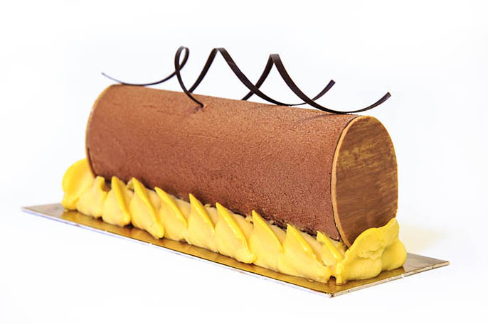 Gâteau cylindrique au chocolat avec une garniture jaune et décor de chocolat noir — photo culinaire à Mâcon