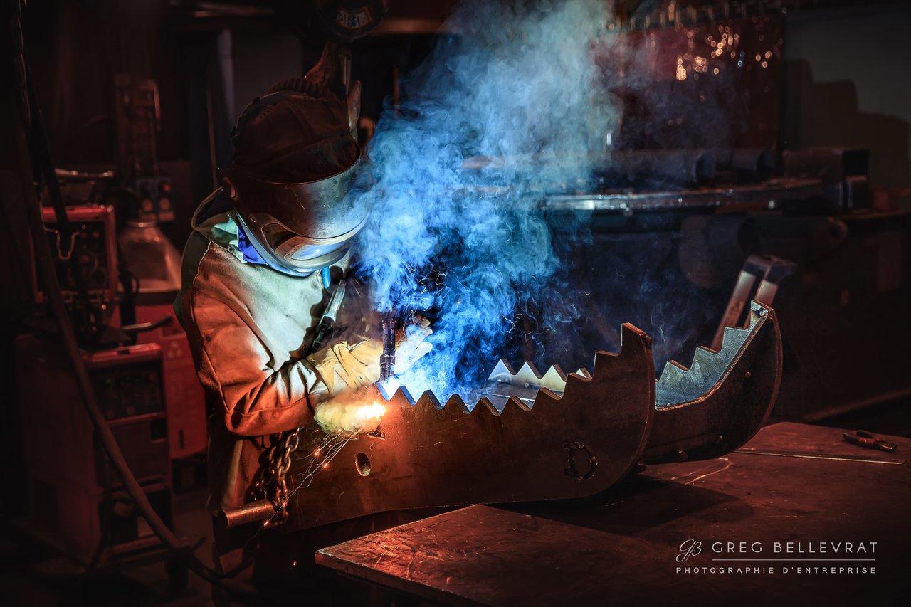 Ouvrier soudeur en casque de protection dans un atelier industriel, avec étincelles et fumée bleue — photographie industrielle à Mâcon
