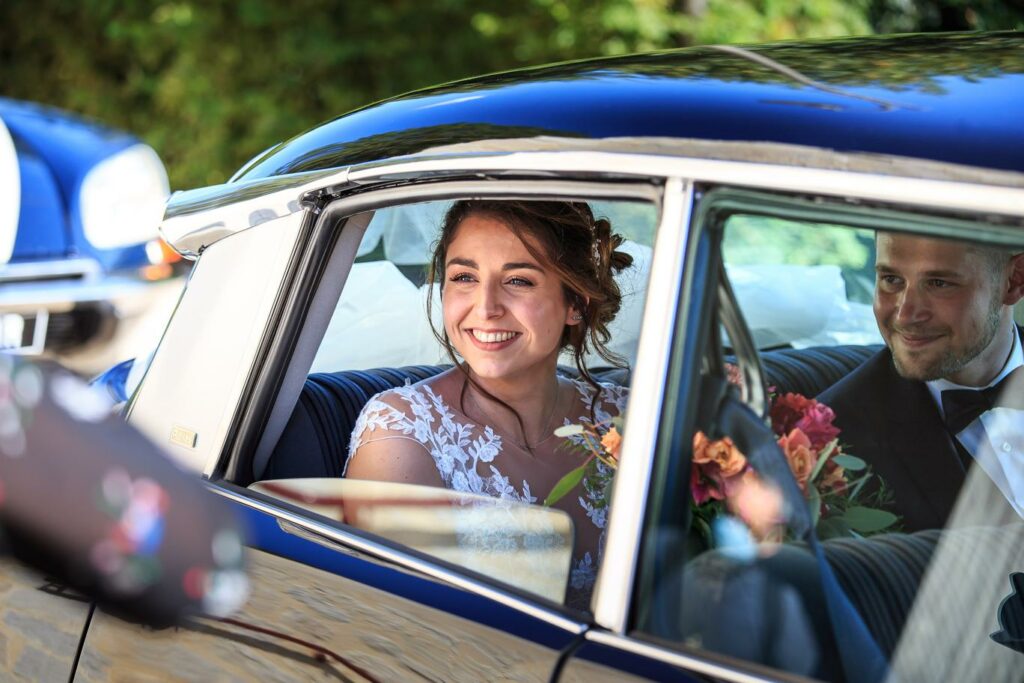 Mariée souriante à bord d'une voiture ancienne avec son bouquet — photographe de mariage à Paray-le-Monial