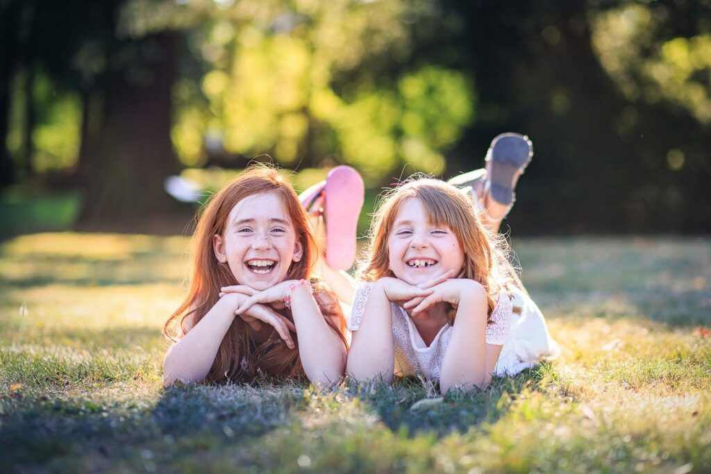 Deux sœurs allongées dans l'herbe en plein fou rire — photographe de famille à Paray-le-Monial