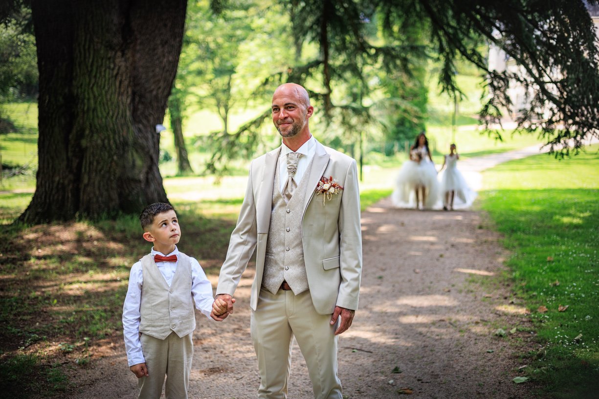 Le marié attend avec leur fils pendant que la mariée approche avec sa fille dans le parc du chateau