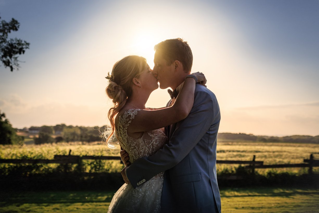 Amandine et Vincent s'embrassent devant la prairie au soleil couchant, mariage a la Ferme du Tremblay