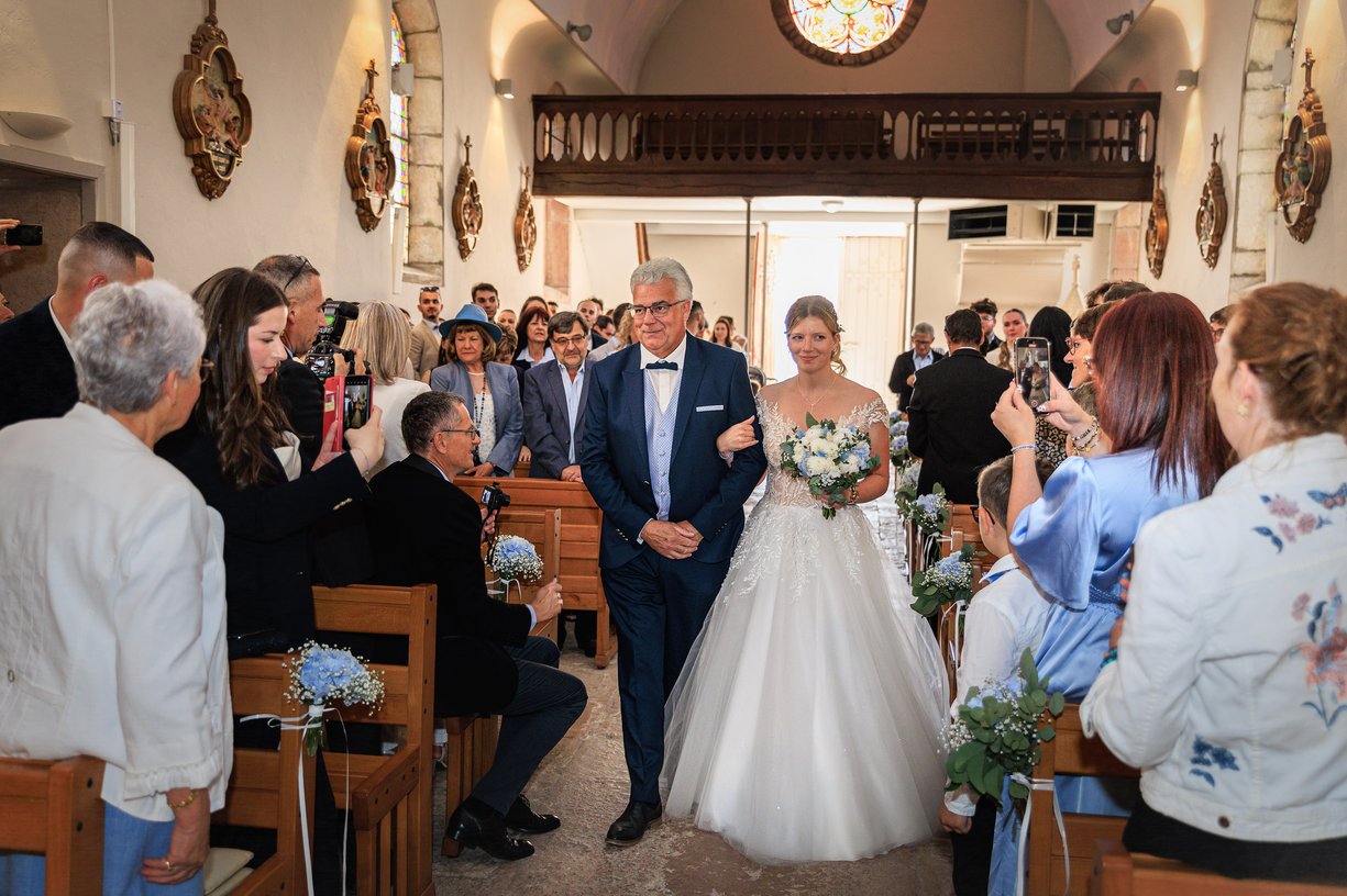Amandine entre dans l'eglise au bras de son pere, bouquet d'hortensias bleus, invites de chaque cote de l'allee