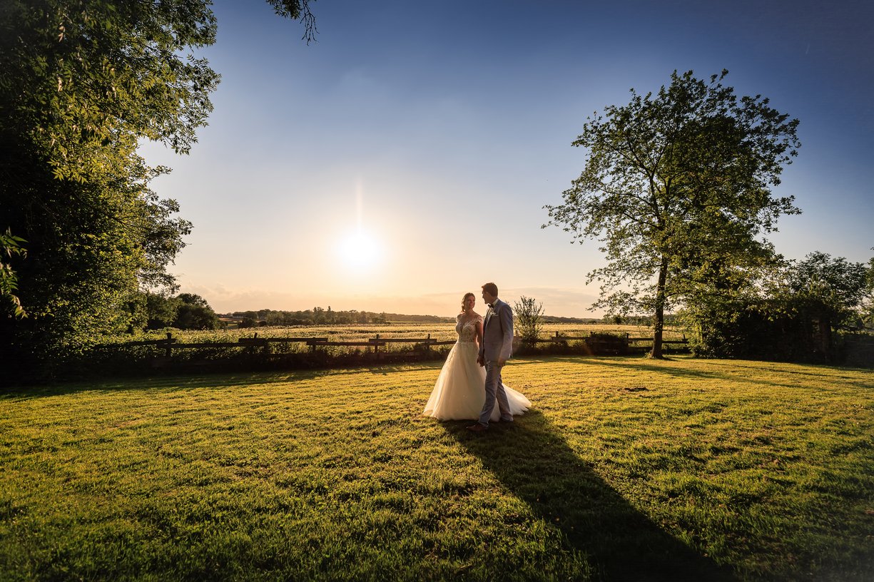 Amandine et Vincent main dans la main au milieu de la prairie au soleil couchant a la Ferme du Tremblay