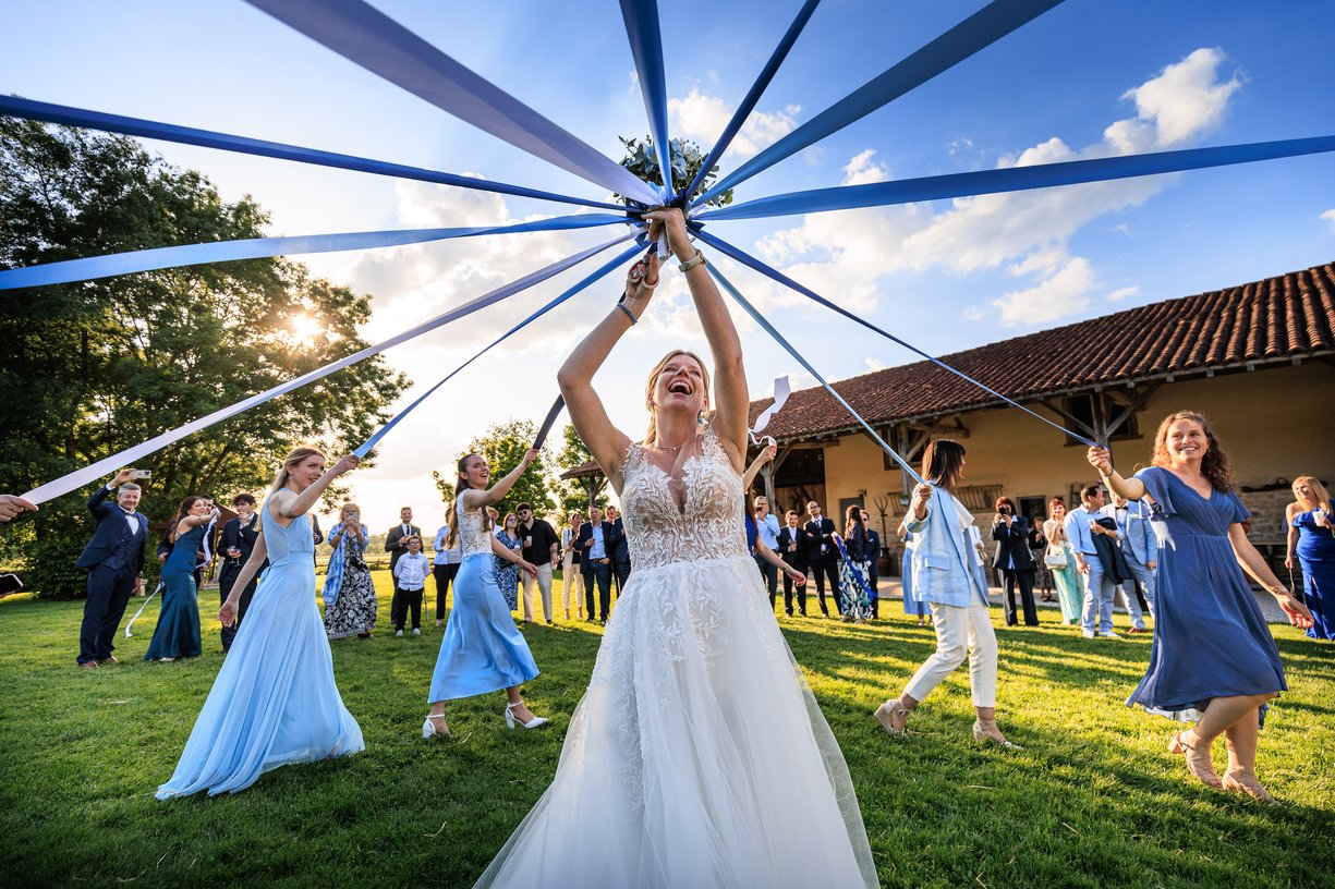 Amandine rit bras leves au centre des rubans bleus du jeu du bouquet, devant la ferme du Tremblay
