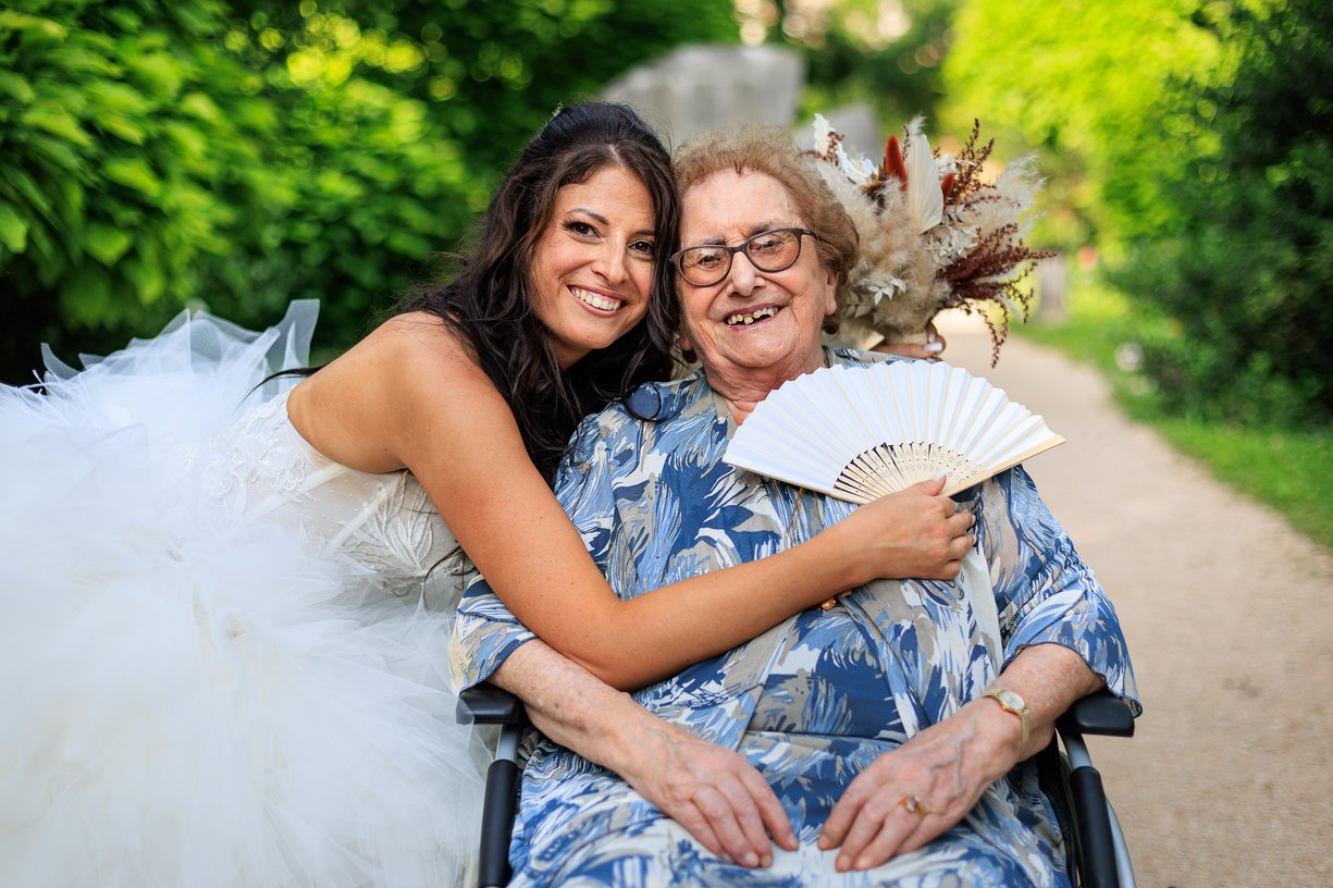 La mariee enlace sa grand-mere en fauteuil roulant pendant le vin d'honneur
