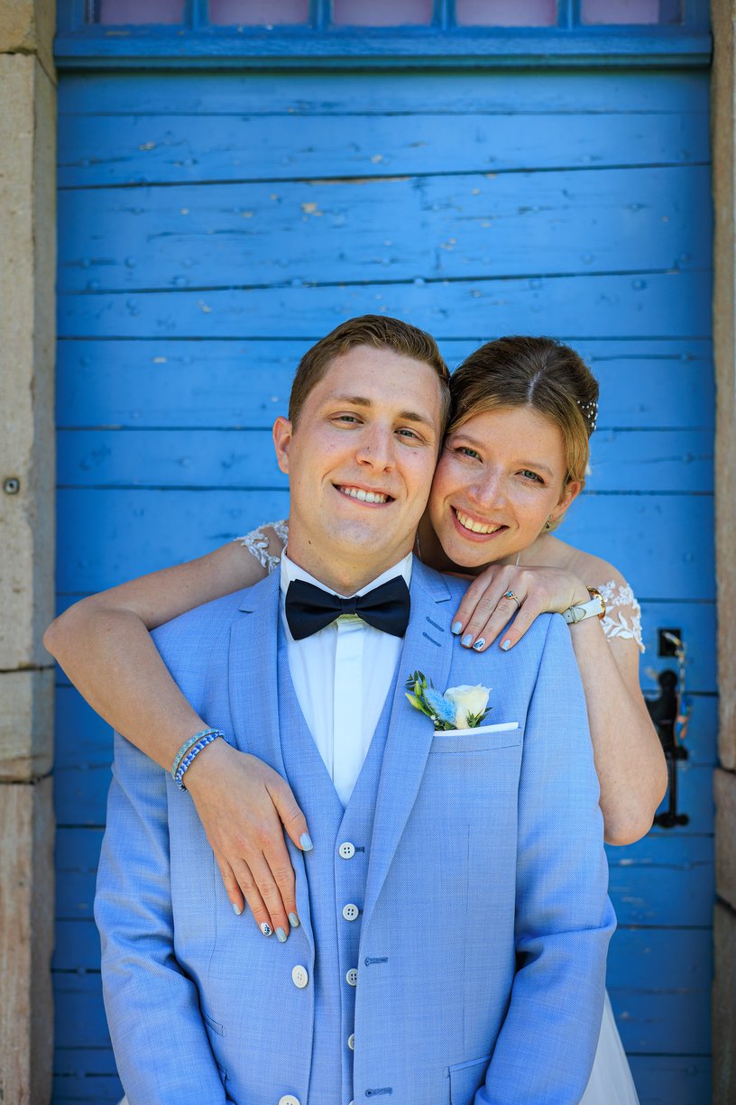 Amandine et Vincent souriants devant la porte en bois bleue de la Ferme du Tremblay