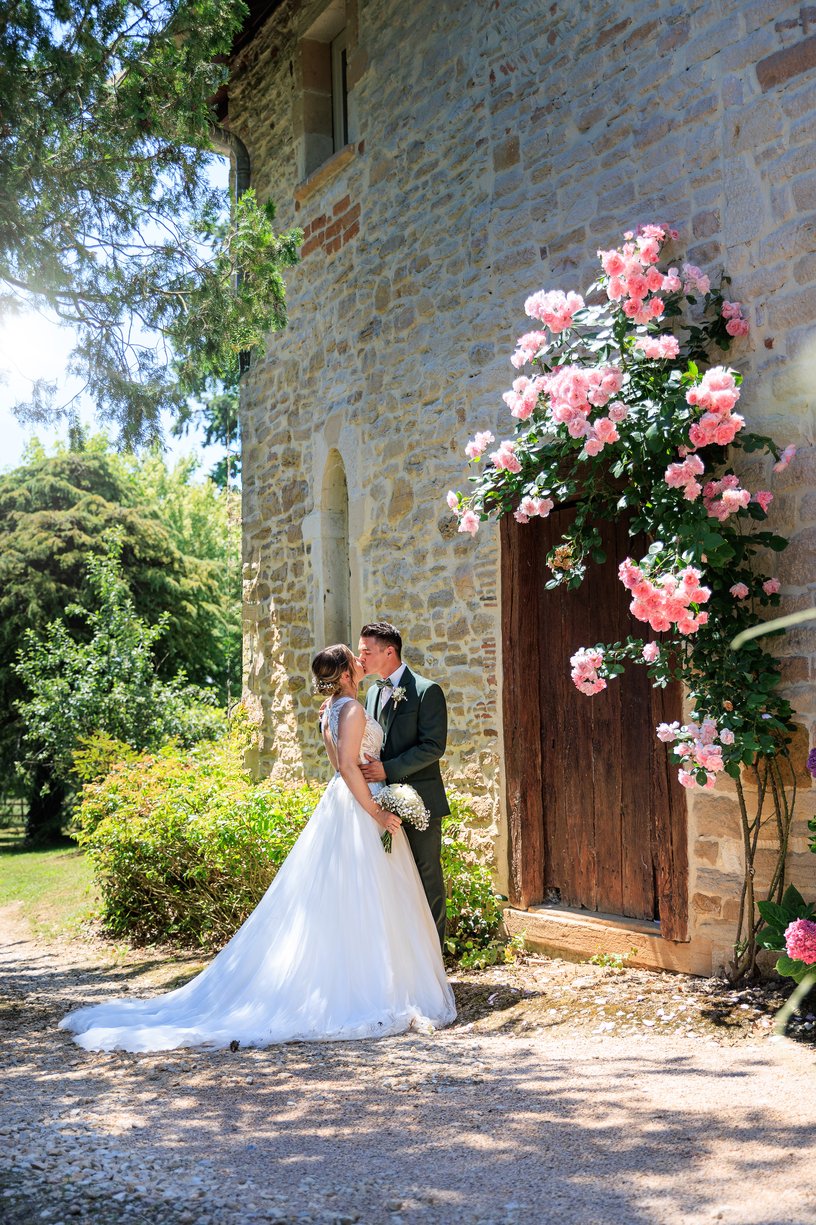 Camille et Dimitri s'embrassent devant une vieille porte en bois couverte de roses roses