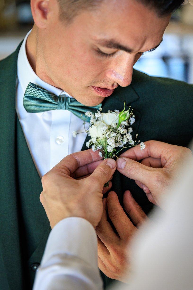 On epingle la boutonniere de roses blanches sur le costume vert de Dimitri