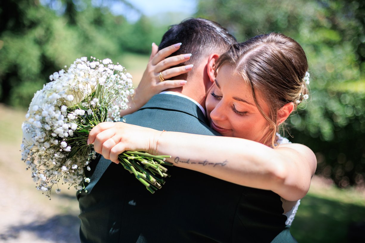 Camille serre Dimitri dans ses bras, yeux fermes, bouquet de roses blanches au premier plan