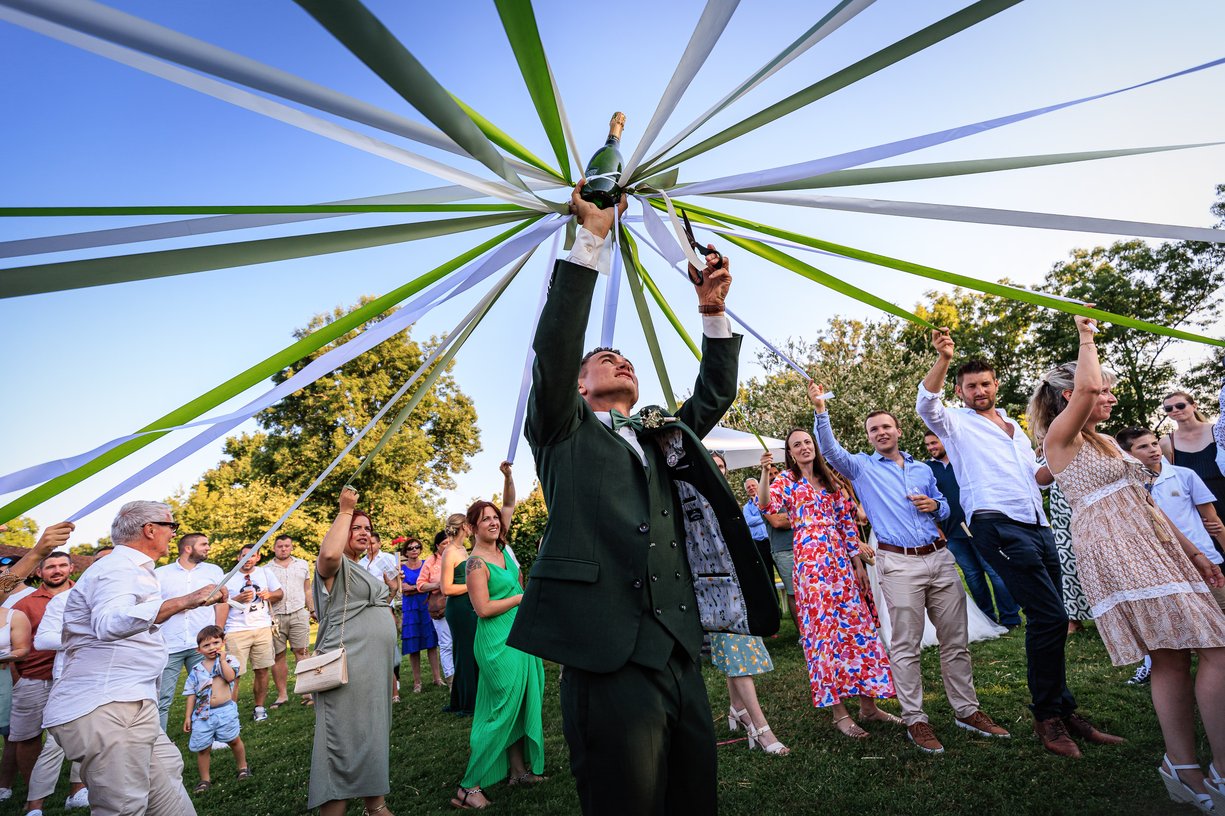 Un invite leve une bouteille de champagne entouree de rubans verts et blancs pendant le jeu du vin d'honneur