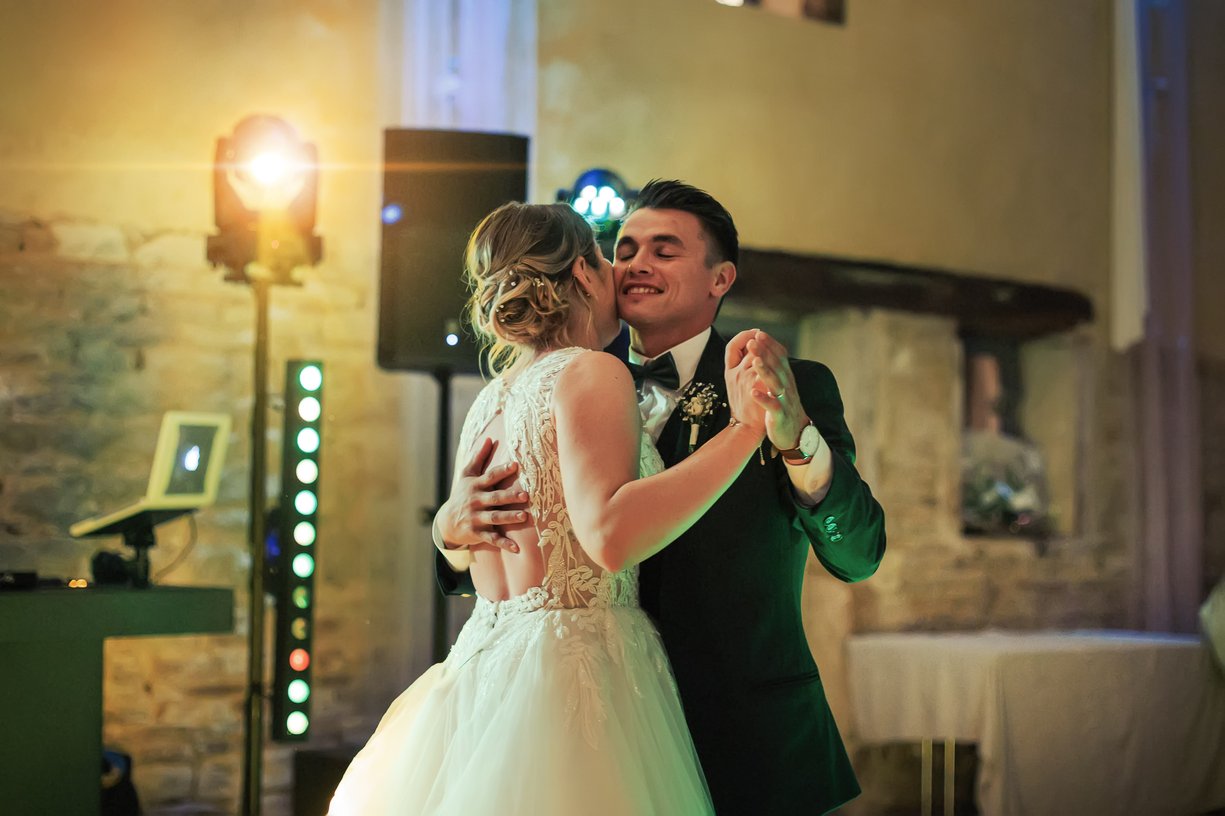 Camille et Dimitri dansent joue contre joue sous les projecteurs colores pendant l'ouverture de bal
